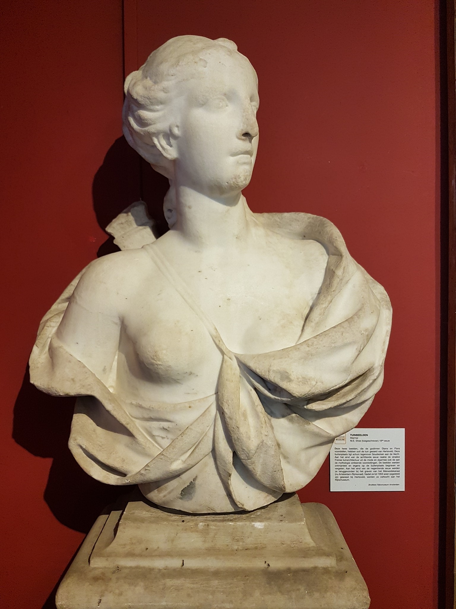 marmeren borstbeeld van een vrouw tegen een rode achterwand, afkomstig uit de tuin van Goudestein